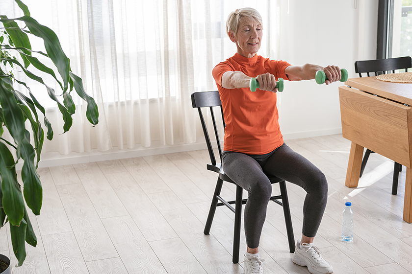 Smiling beautiful senior woman health instructor doing chair exercises